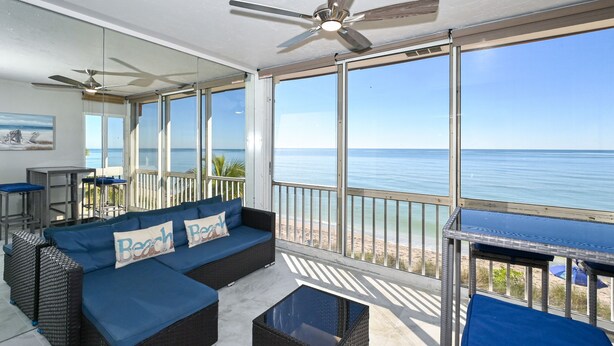 A balcony with a view of the ocean, a blue sofa with 'Beach' pillows, and a ceiling fan. - Beachfront Condo - 3 BR- Heated Pool - Free Boat Docks – Upscale – Siesta Key (Siesta Key)