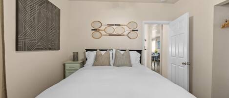 A bedroom with a bed, a nightstand, a wall-mounted tennis racket display, and a door leading to another room.