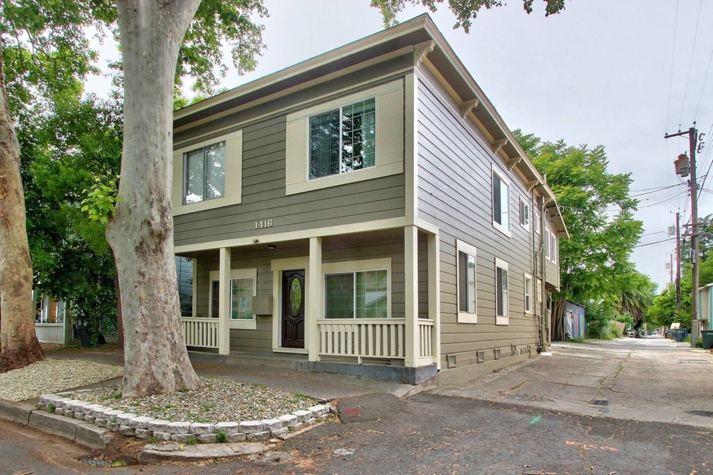 Une maison à deux étages avec un porche à l’avant, un garage et un grand arbre devant.
