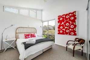 A bedroom with a bed, bedside table, lamp, chair, and a large window.