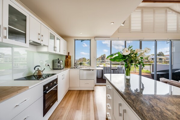 A modern kitchen with white cabinetry, a built-in oven, and a large window offering a view of the outdoors. - Luxury @ Hayborough Enjoy Sea, Town & Island Views Hot tub, Woodfire & Firepit   (Hayborough)
