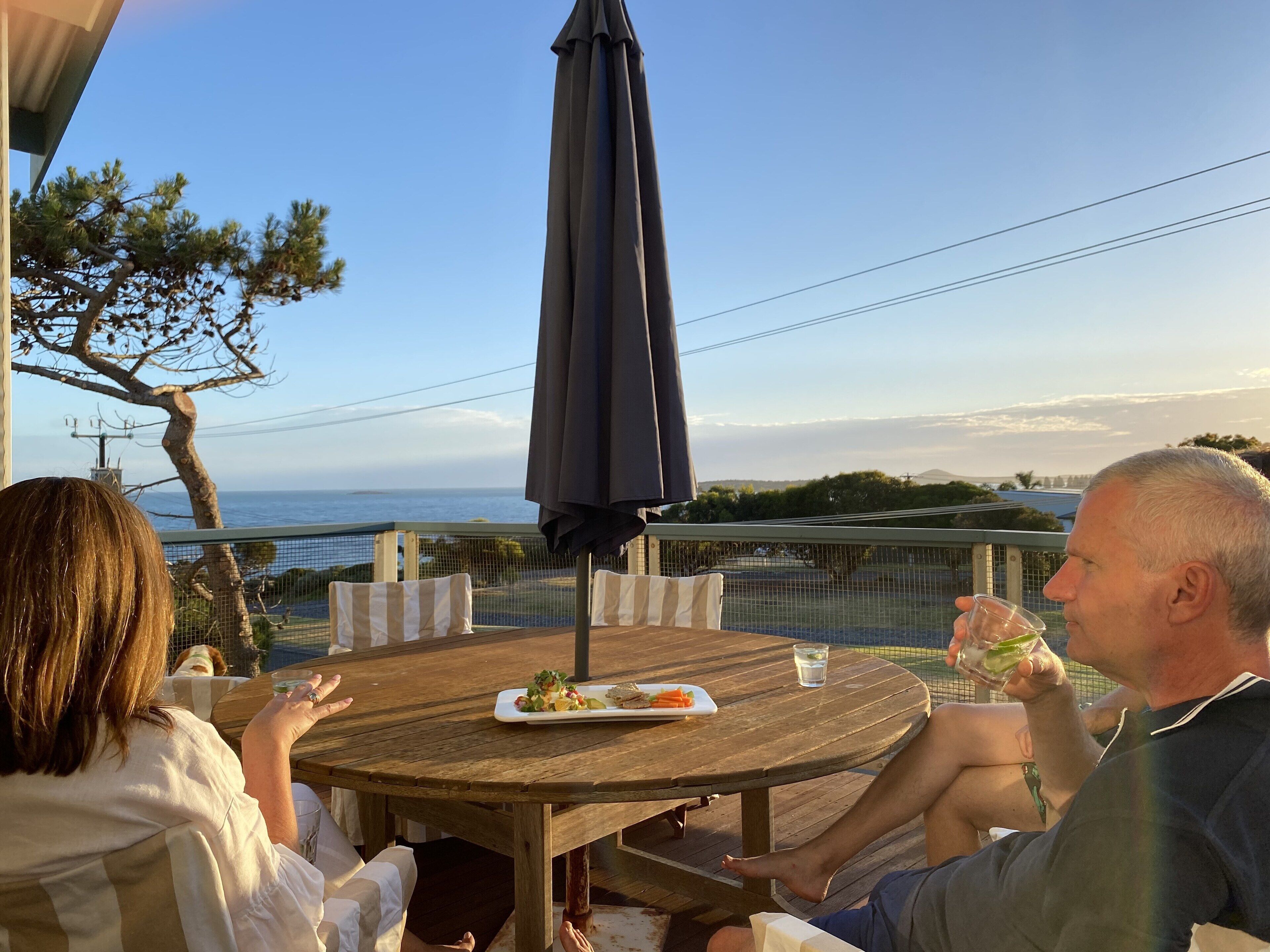 A wooden table with a plate of food and a glass of water, set outdoors with a view of the sea.