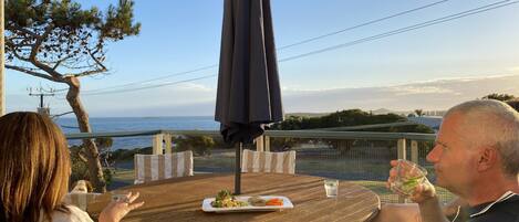 A wooden table with a plate of food and a glass of water, set outdoors with a view of the sea.