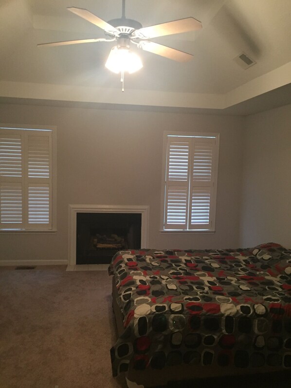 A bedroom with a ceiling fan, two windows with blinds, a fireplace, and a bed with a patterned bedspread. - Masters rental half mile from course!! (Augusta)