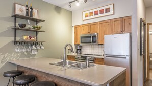 A modern kitchen with a central island, stainless steel appliances, wooden cabinets, and a bar stool area. -  Location, Location, Location! Large Corner Ground Floor Newly Renovated Condo (Silver Star Mountain)