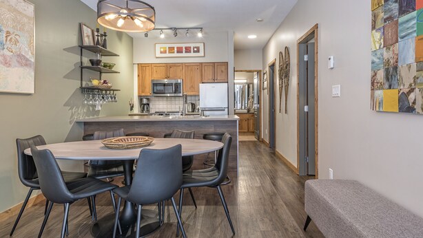 A modern kitchen with wooden cabinets, a central island, and a dining area with a round table and chairs. -  Location, Location, Location! Large Corner Ground Floor Newly Renovated Condo (Silver Star Mountain)