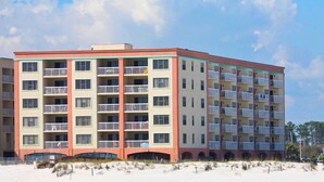 Un hôtel à plusieurs étages doté de balcons, offrant une vue sur la plage et dont le rez-de-chaussée est recouvert de sable.