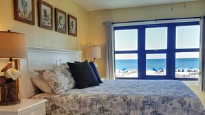 Une chambre à coucher avec un lit, une table de chevet, une lampe et une vue sur la plage.