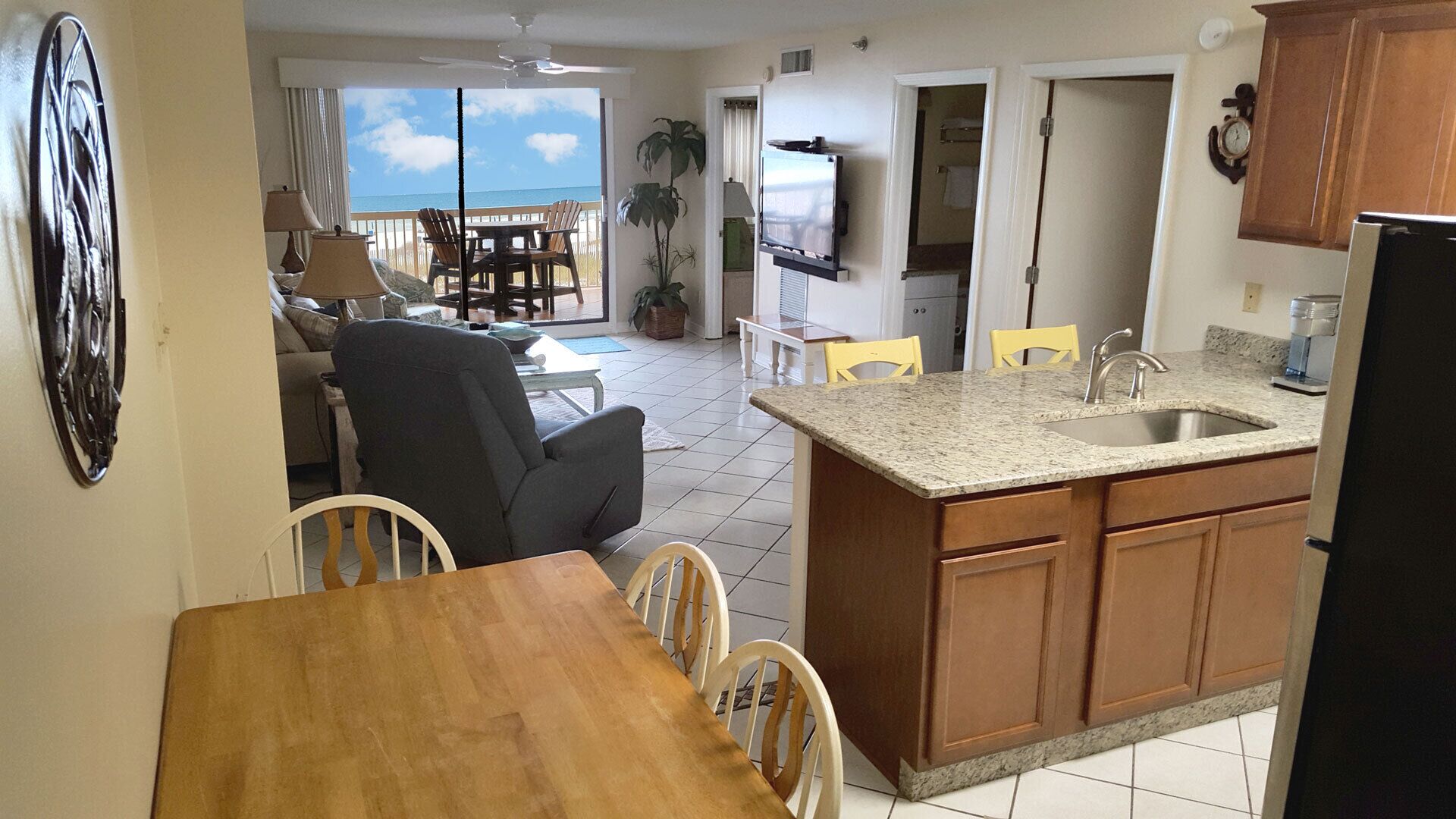 A kitchen with a granite countertop, wooden cabinets, and a stainless steel sink. There is a dining area with a wooden table and chairs.
