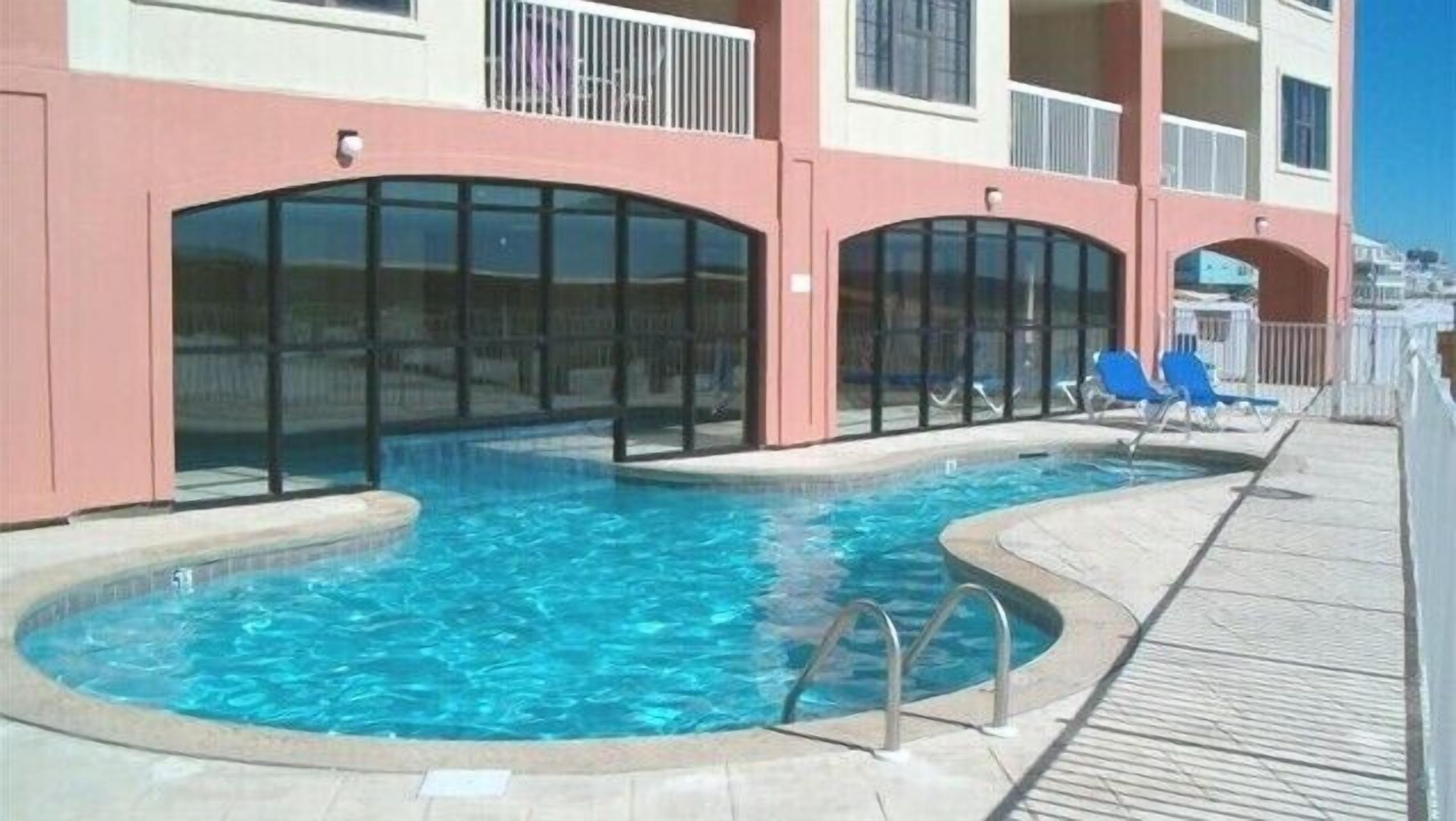 A swimming pool with a deck, surrounded by a building with balconies and large windows.