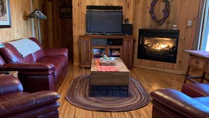 A wooden-paneled living room with a leather sofa, a television, a fireplace, and a rug. - Tennessee's Finest Smoky Mountain Vacation Rental Getaway!  (Townsend)