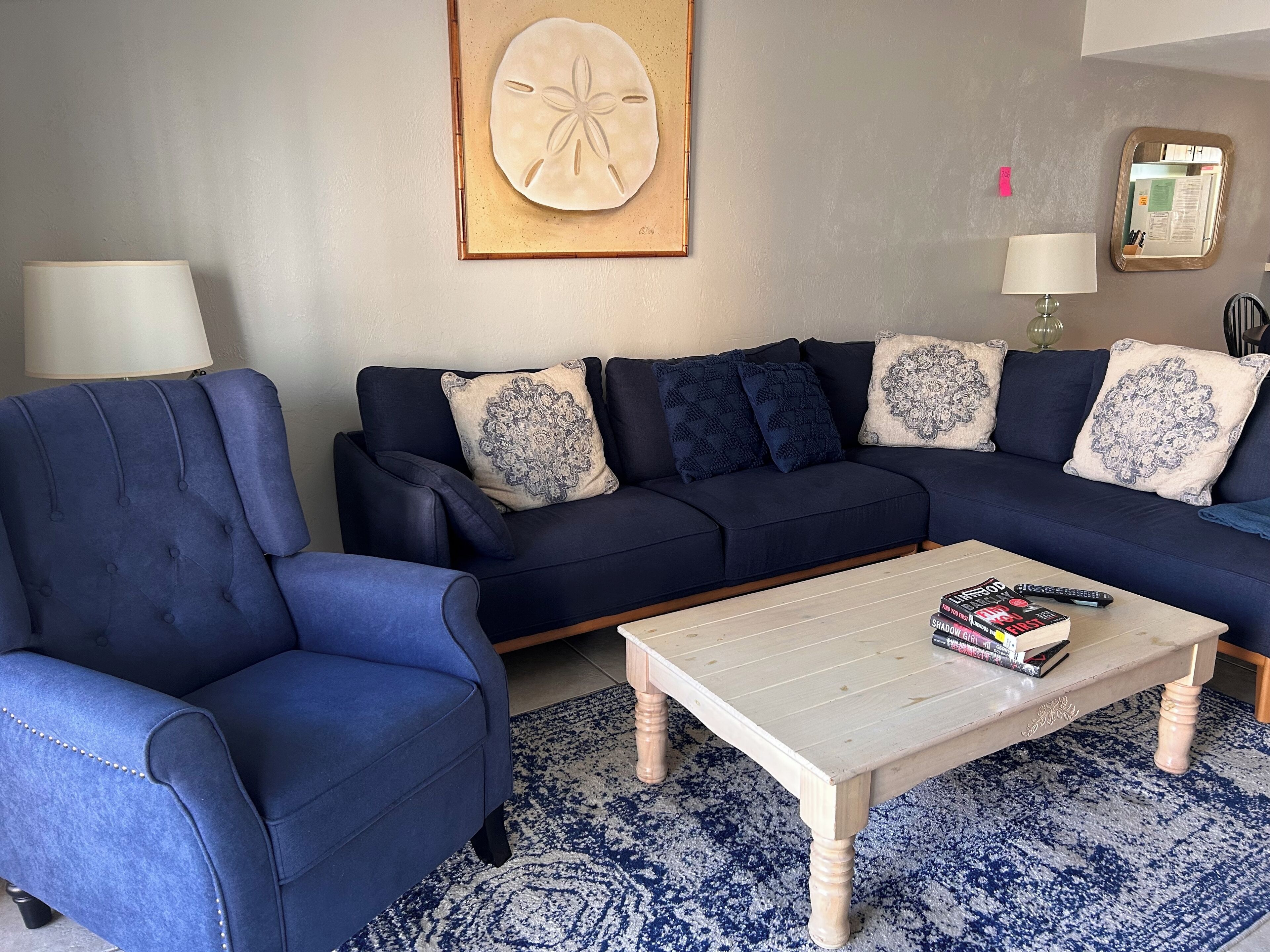 Un salón con un sofá azul oscuro, un sillón a juego, una mesa de centro con libros y una alfombra estampada.