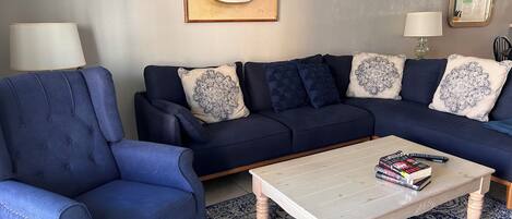 Un salón con un sofá azul oscuro, un sillón a juego, una mesa de centro con libros y una alfombra estampada.
