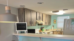 Eine moderne Küche mit Holzausstattung, einer weißen Arbeitsplatte und einem Kreidetafel-Schild. Es gibt eine Essecke mit einem runden Tisch und vier Stühlen.
