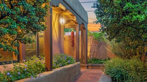 A covered outdoor area with a brick pathway, surrounded by greenery and a hanging plant.