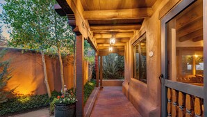 A covered walkway with a brick path, wooden ceiling, and a large potted plant.