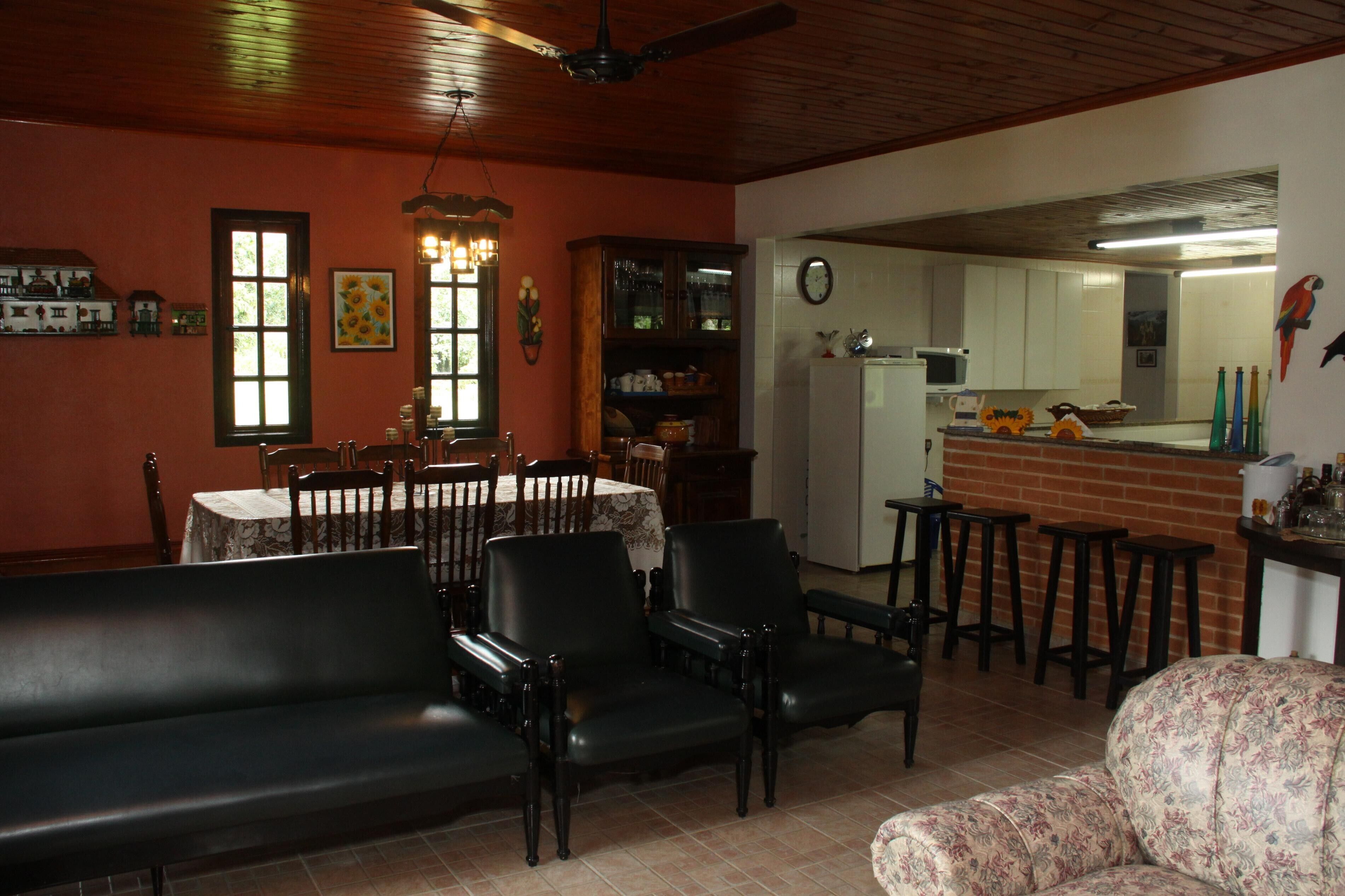A dining area with a table and chairs, a sofa, and a kitchen area with a refrigerator and bar stools.