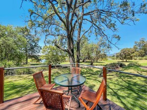 Enjoy a serene outdoor space with a glass-top table and comfortable seating, overlooking a beautifully manicured lawn and a distant view of rolling hills.
