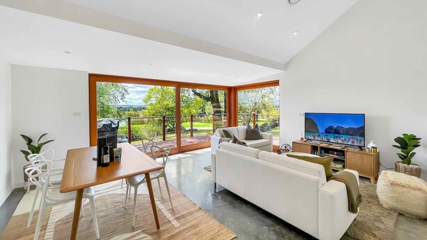 A modern living room with a white sofa, a dining table, and a TV.