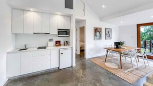 A modern kitchen with white cabinets, a microwave, and a coffee maker. There is a dining area with a wooden table and chairs.