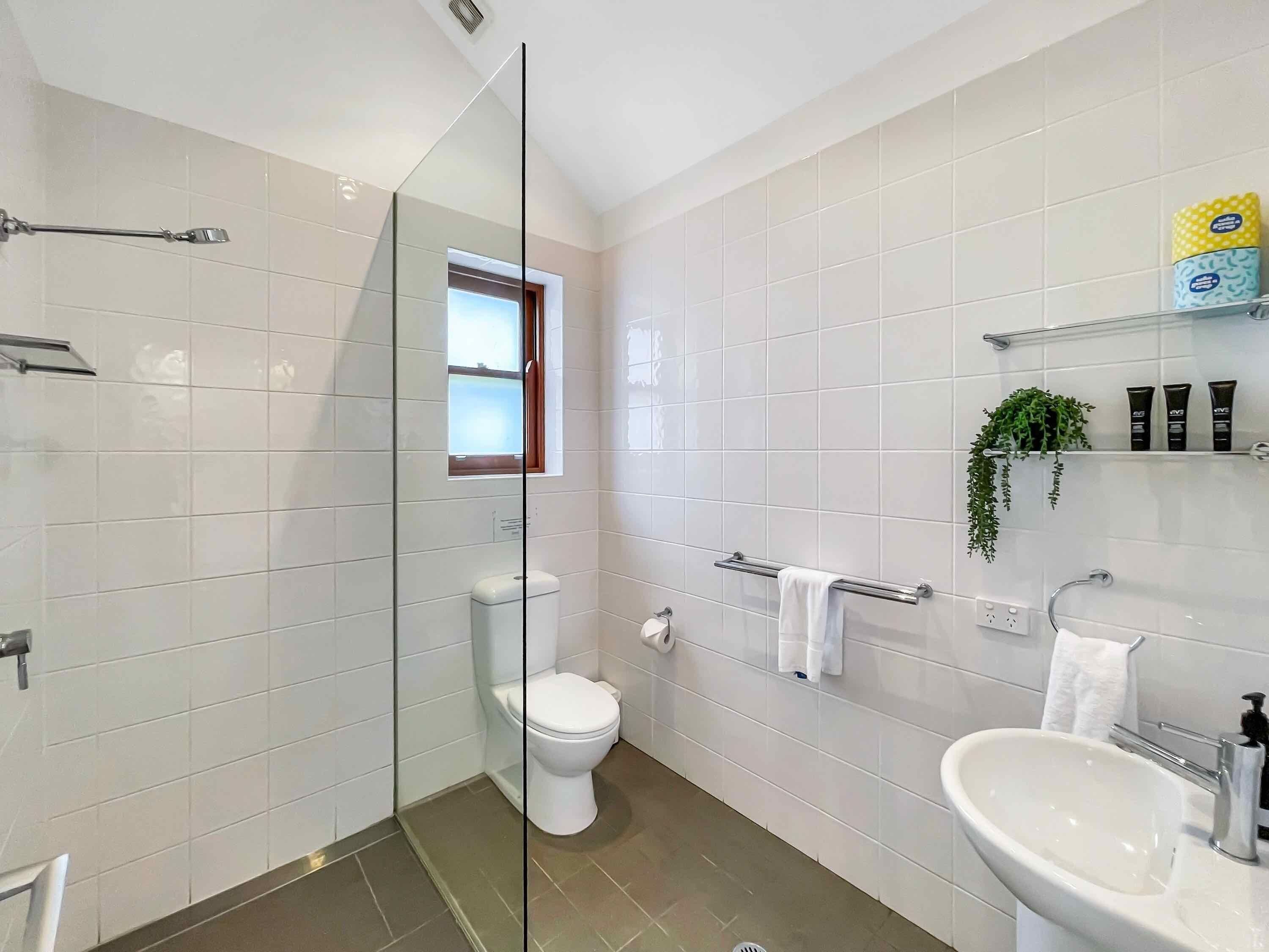 A modern bathroom with a glass shower enclosure, a toilet, a sink, and a window.