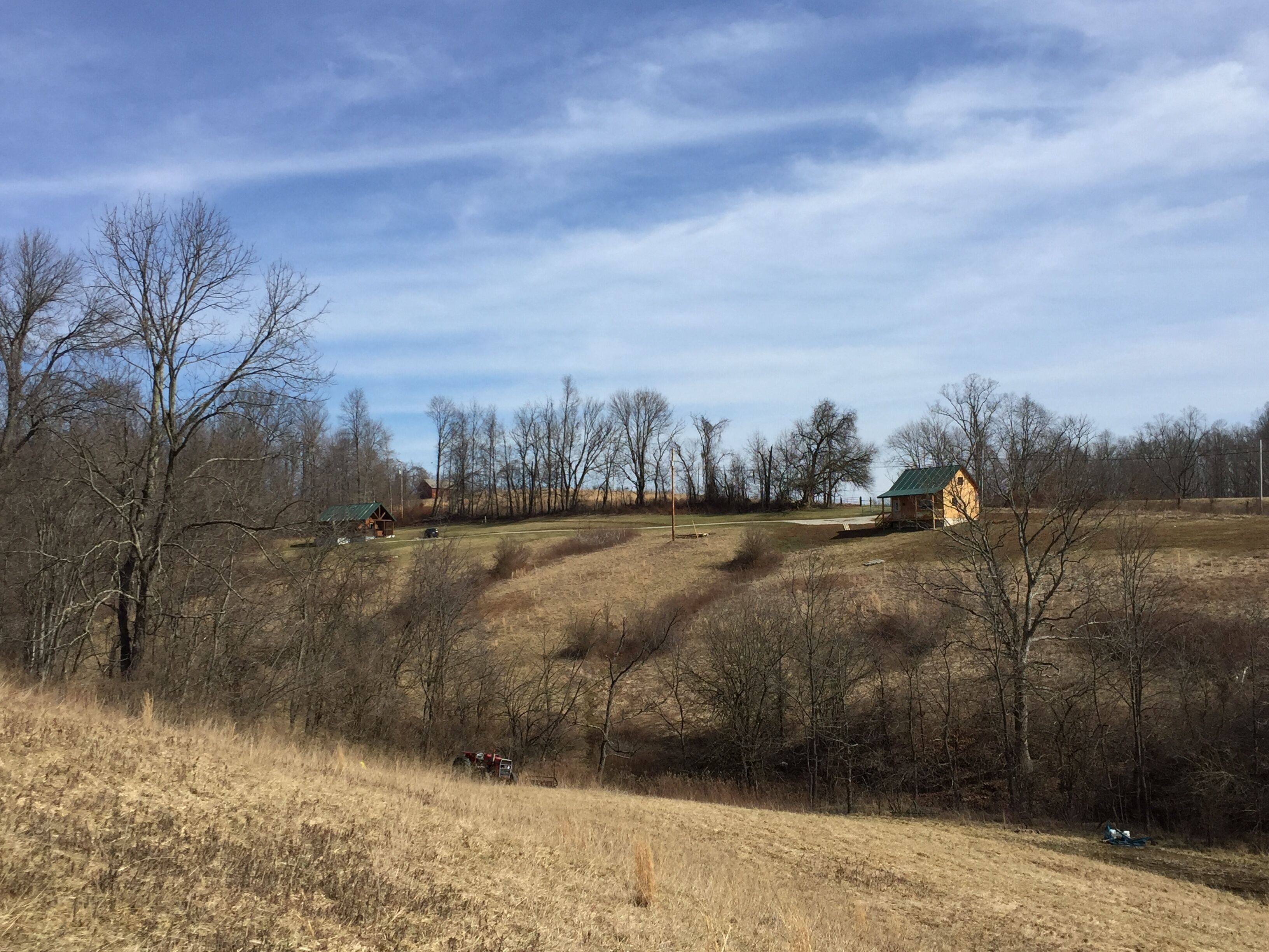 A rural landscape with a small wooden cabin, open fields, and leafless trees.