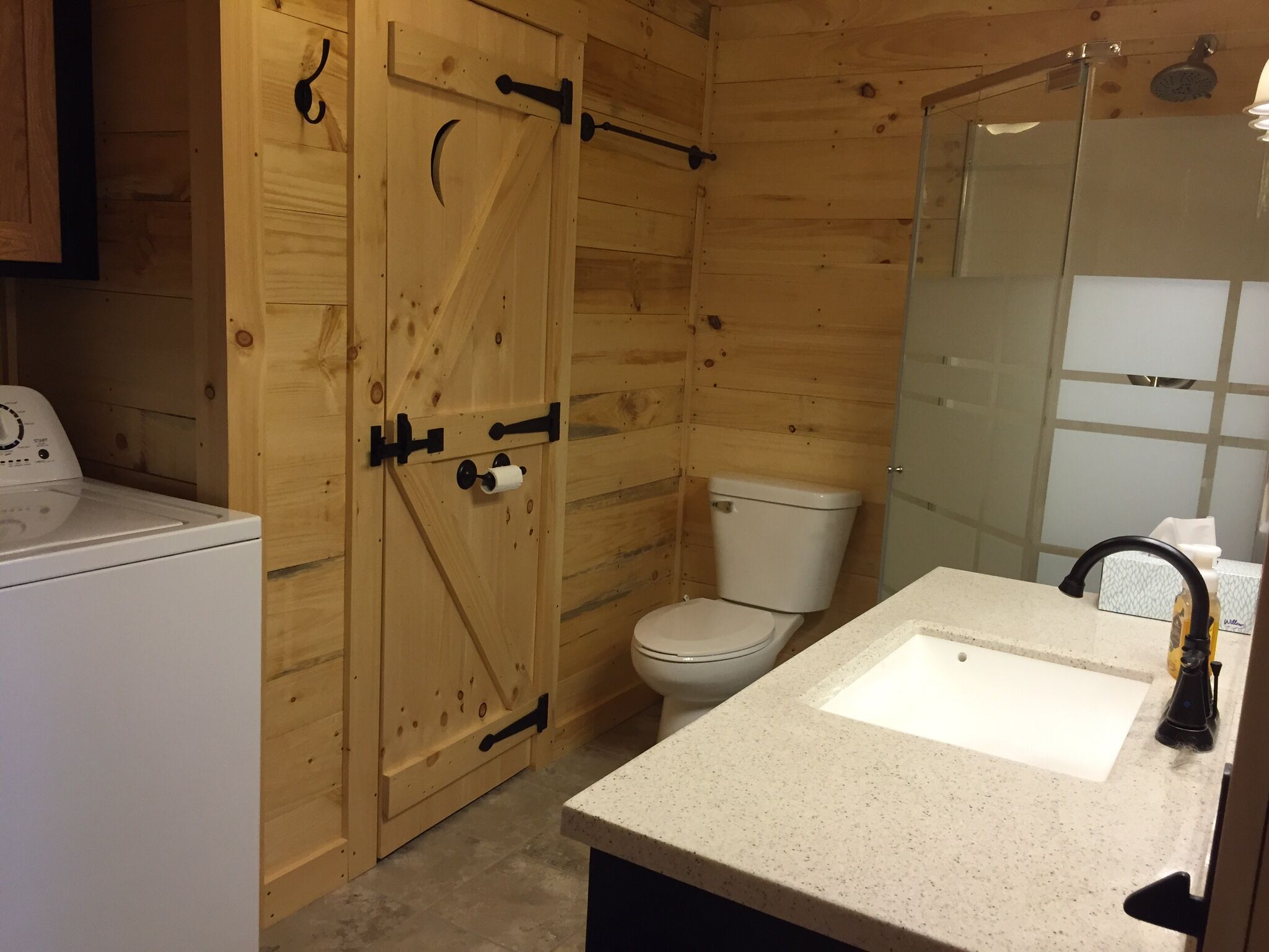 Een kleine houten badkamer met toilet, wastafel en douche.