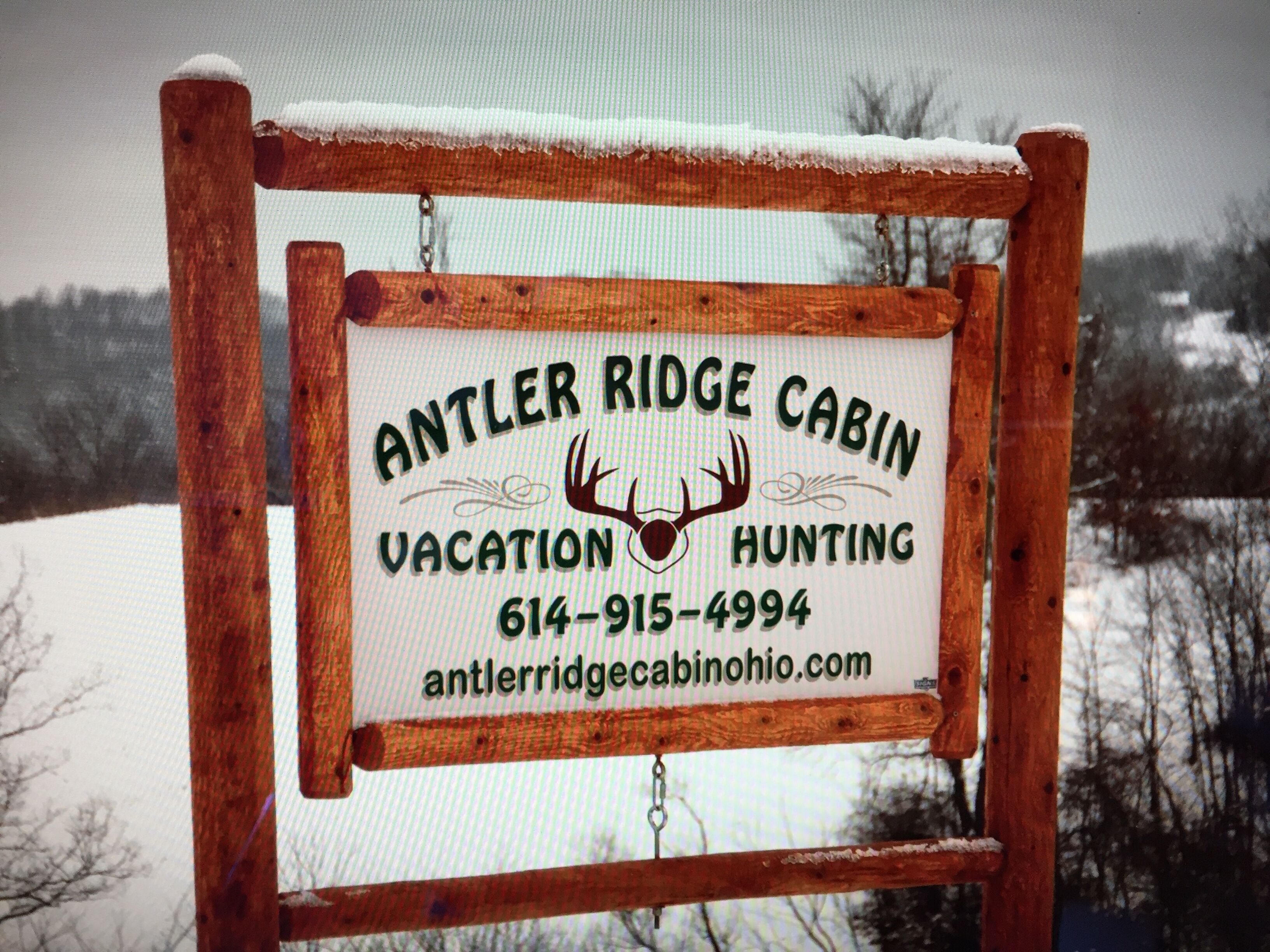 Een houten bordje met de naam 'Antler Ridge Cabin' en contactgegevens.
