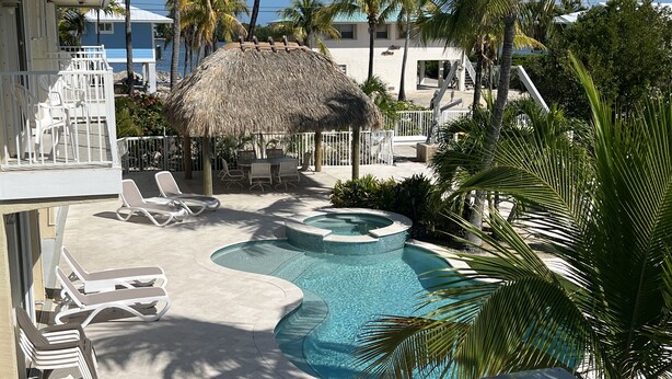 A pool area with lounge chairs, a thatched-roof structure, and palm trees. - Open Water views, 80' dock Private Pool Ice machine DIRECT ACCESS  open water (Marathon)
