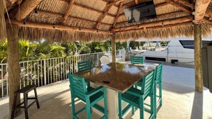 A covered outdoor area with a thatched roof, a table with chairs, and a view of a boat in the background. - Open Water views, 80' dock Private Pool Ice machine DIRECT ACCESS  open water (Marathon)
