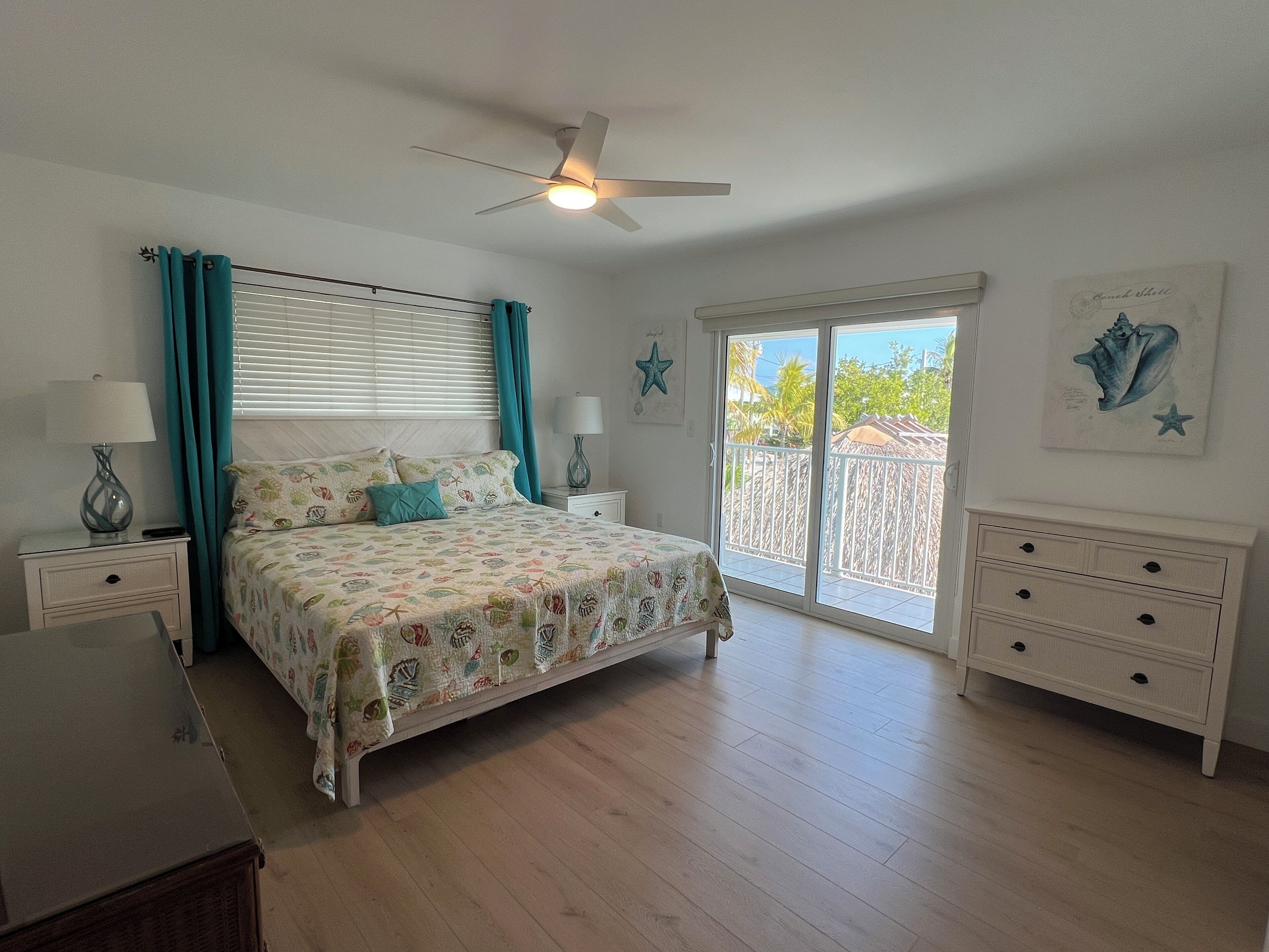 A bedroom with a bed, nightstands, a dresser, a ceiling fan, and a view of the outdoors.