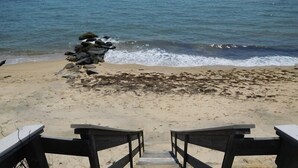 Eine Holztreppe führt zu einem Sandstrand mit einem Felsen im Wasser.