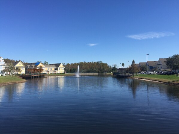 Un lago tranquilo con una fuente, rodeado de edificios residenciales y un cielo despejado.