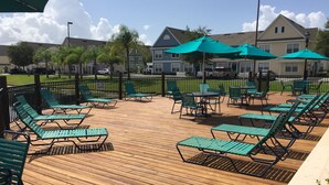 A wooden deck with green lounge chairs and umbrellas, surrounded by a fence and houses in the background. - 25 minutes to Disney World! Family-sized townhouse (Kissimmee)
