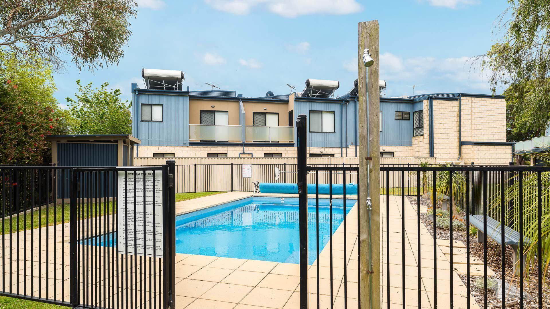 Un immeuble résidentiel doté d’une piscine, d’un espace clôturé et d’un poteau en bois.