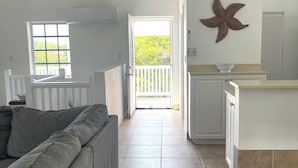 En rummelig opholdsstue med en grå sofa, et køkken med en hvid bordplade og en balkon med gelænder i hvid.