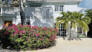Et hvidt toetagershus med balkon, omgivet af frodigt grønt og pink bougainvilleablomster.