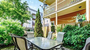 An outdoor patio with a glass-top table and chairs, surrounded by lush greenery and a wooden fence. - Fall In Love With Portland! (Portland)