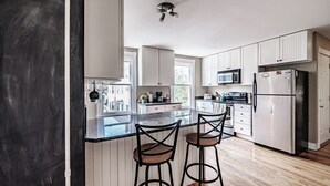 A modern kitchen with white cabinets, a black countertop, and two bar stools. - Fall In Love With Portland! (Portland)