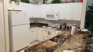 Una cocina con armarios blancos, un refrigerador de acero inoxidable, un microondas, una estufa y una encimera de granito.