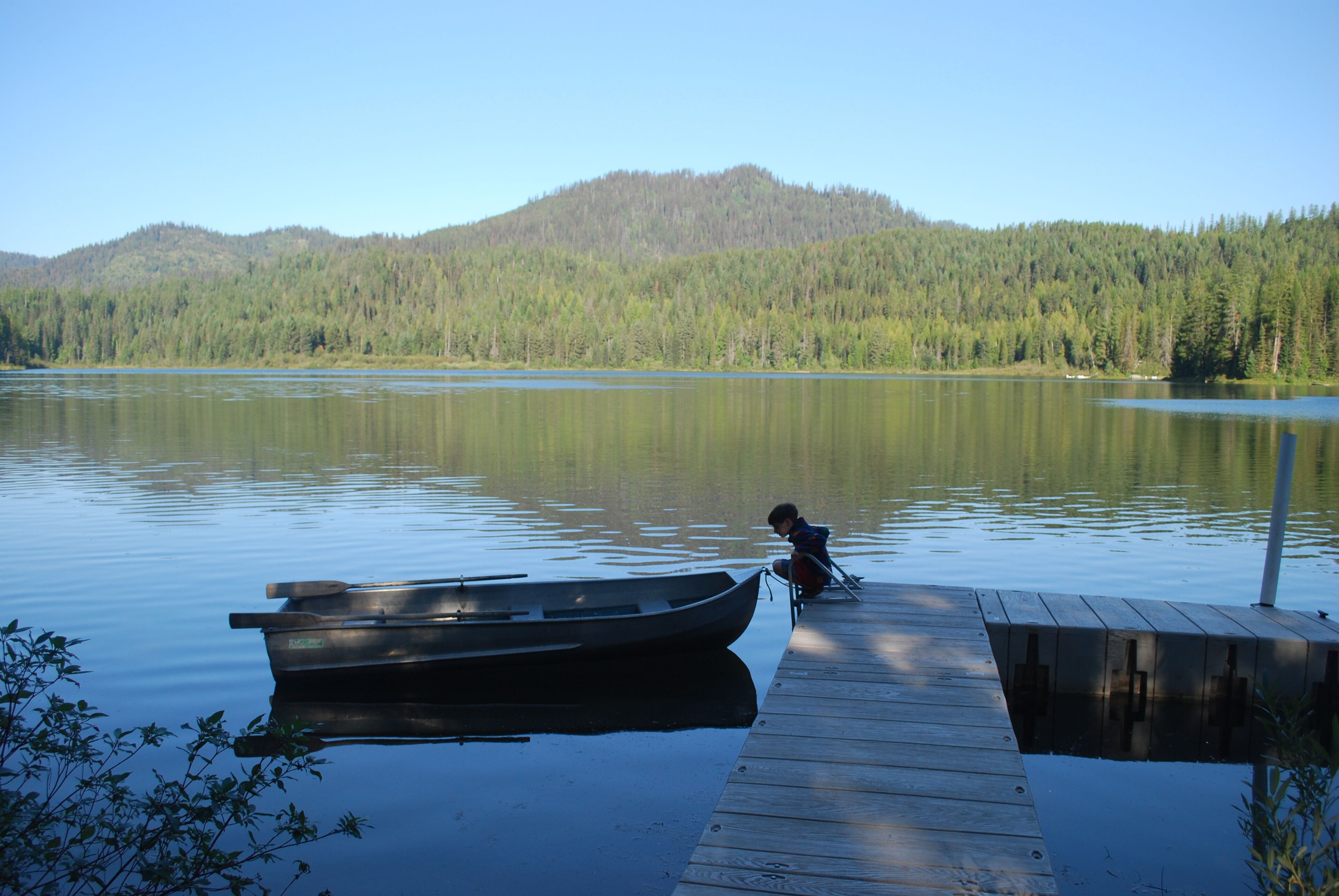 A wooden dock extending into a calm lake with a boat moored at the end.