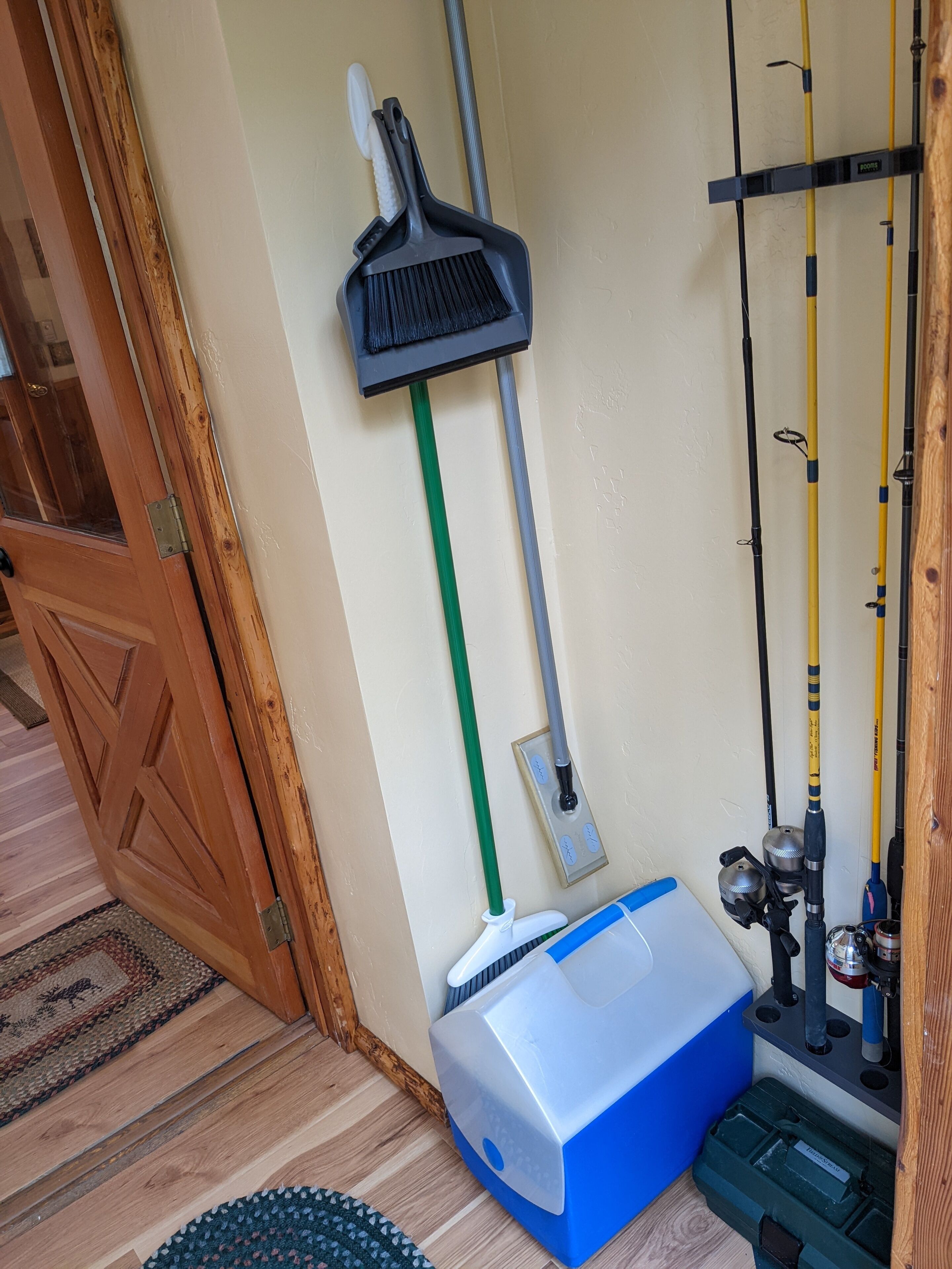 Una habitación con una puerta de madera, un escoba, un trapeador, cañas de pescar y un carrito de limpieza azul y blanco.