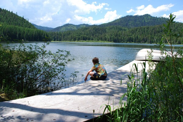 A wooden dock extending into a lake with a forested mountain in the background.