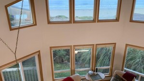 A room with multiple large windows offering ocean views, a small round table, and two sofas. - Pacific Panorama - 5 bedrooms + loft (Bandon)
