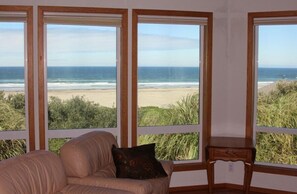 Une pièce avec vue sur la plage, grâce à de grandes fenêtres, comprenant un canapé beige et une petite table en bois.