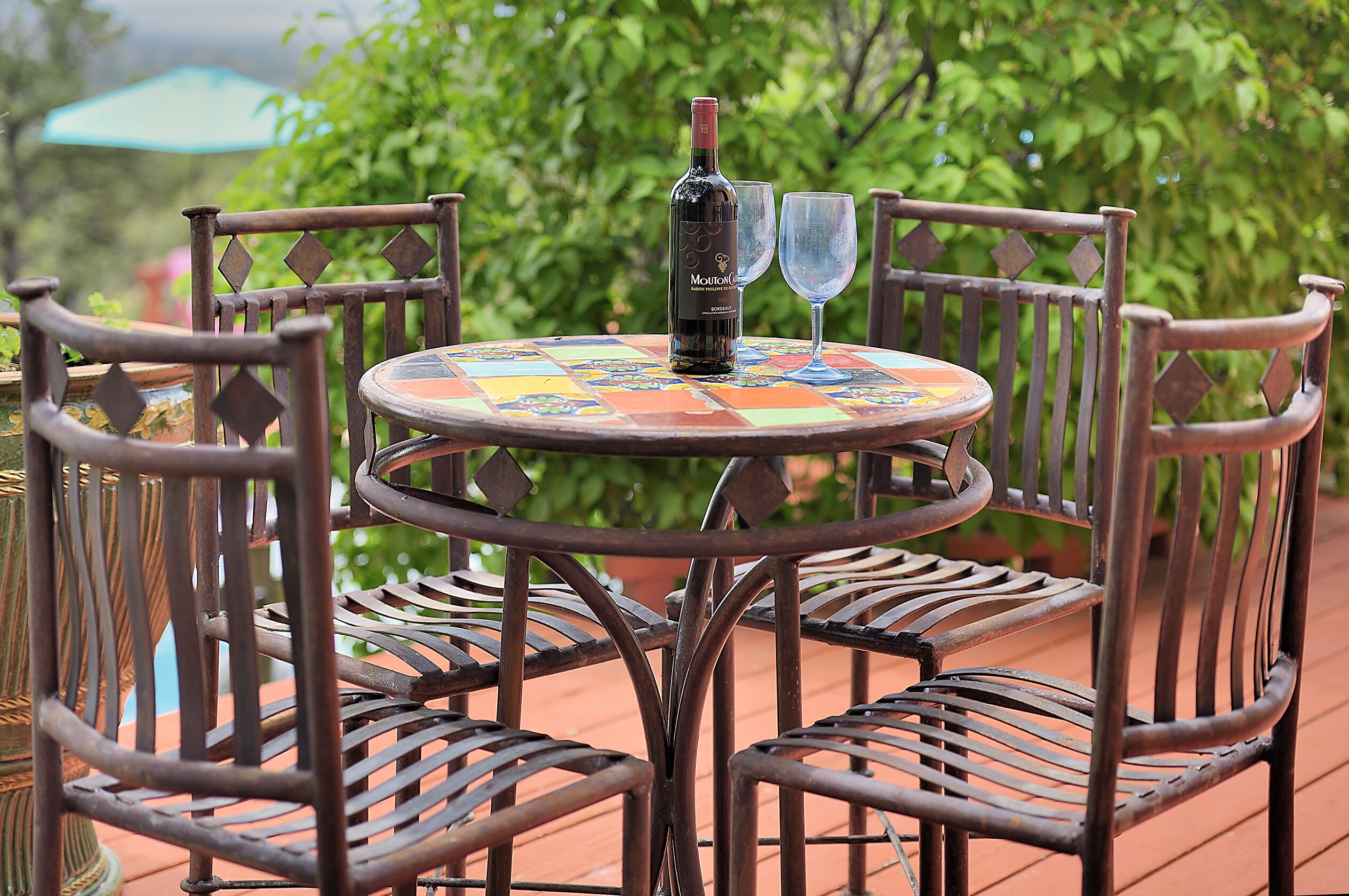 A round metal table with a colorful tiled top, surrounded by metal chairs with a lattice backrest design.