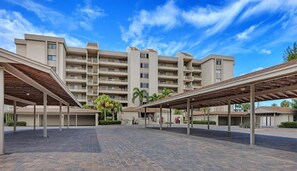 A multi-story hotel with a covered outdoor area, palm trees, and a clear blue sky.