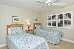 Ein Schlafzimmer mit zwei Betten, einem Deckenventilator und einem Fenster mit Rollläden.