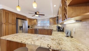A kitchen with wooden cabinets, a granite countertop, a ceiling fan, pendant lights, and a large island.