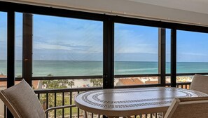 En balkon med udsigt over havet, et rundt bord og to stole.